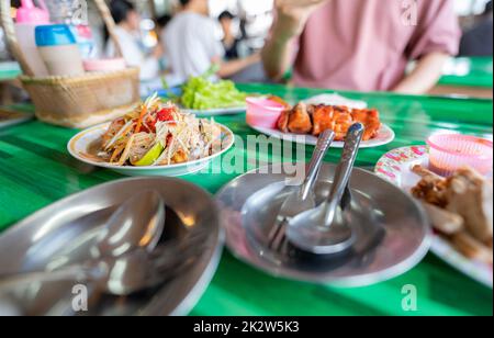 Würziger grüner Papayasalat oder Som TUM mit thailändischen Reisnudeln. Street Food mit heißem und würzigem Gericht in Thailand. Das berühmte lokale thailändische Street Food. Thailändische Esarn-Küche. Papayasalat mit gegrilltem Hähnchen. Stockfoto