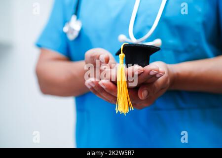Asiatische Frau Arzt hält Abschlusshut im Krankenhaus, Medizinische Ausbildung Konzept. Stockfoto