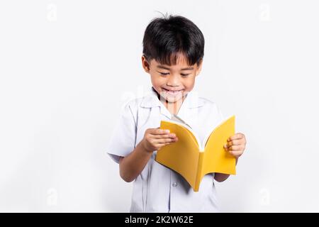 Asiatisches Kleinkind lächelt glücklich und trägt Thai-Uniform, rote Hosen, die stehen und ein Buch lesen Stockfoto