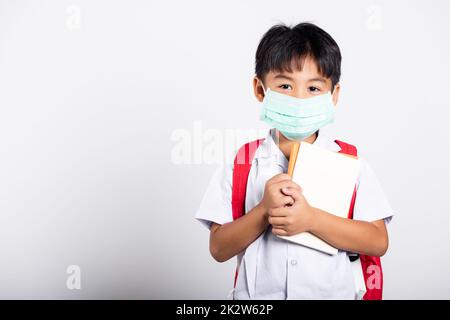 Asiatischer Student Kind Junge trägt Student thai Uniform und medizinische schützen Gesichtsmaske und umarmende Notiz Stockfoto