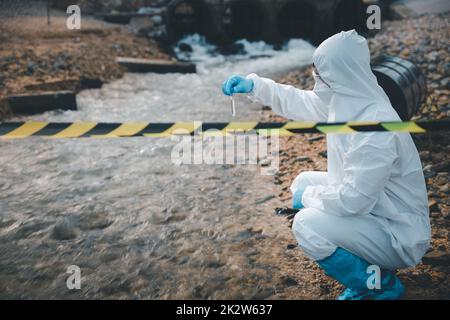 Wissenschaftler oder Biologe in Schutzanzug und Schutzmaske sammelt Abwasserproben aus der Industrie für die Analyse Stockfoto