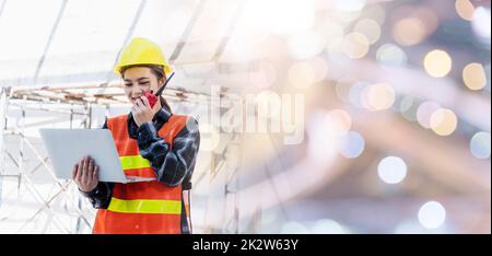 Eine Mitarbeiterin einer asiatischen Ingenieurin, die auf einer Baustelle arbeitet, verwendet einen Laptop und spricht mit dem Radio Stockfoto