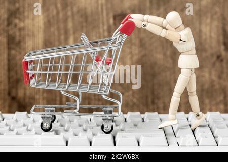Hölzerne Schaufensterpuppe, die leeren Warenkorb auf Computertastatur schiebt Stockfoto