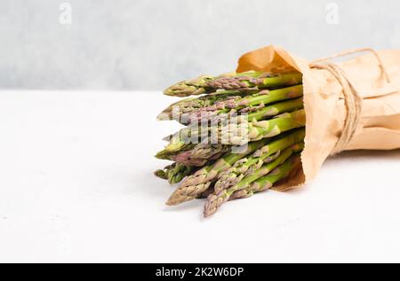 Frisches grünes Spargelbündel auf einem weiß strukturierten Tisch, Gemüse im Frühjahr, Gourmet-Küche, Kochen einer veganen Mahlzeit Stockfoto