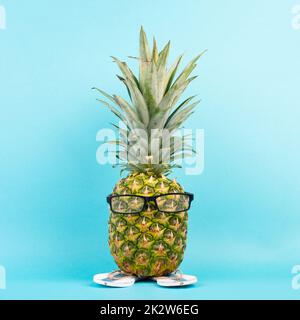Ananas mit Gläsern und Flip Flops, Urlaubs- und Reisekonzept, tropischer Sommerurlaub, lustige Früchte, blauer Hintergrund Stockfoto