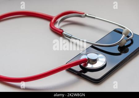 Rotes Stethoskop auf schwarzem Smartphone stellt Gesundheitsdaten und digitale Patientenakten mit mobilen Geräten für digitale Ärzte und digitale diagnostische Behandlung mit modernen Geräten und Technologien dar Stockfoto