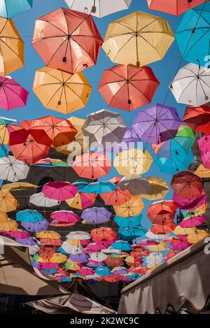 Blick aus dem niedrigen Winkel auf mehrfarbige Regenschirme, die im Sommer zwischen Gebäuden hängen Stockfoto