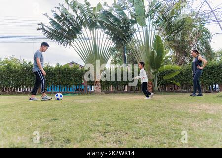 Mutter, Vater und Tochter spielen Fußball in der Natur, einem Gartenpark Stockfoto