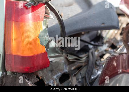 Eine rote und orangefarbene zerbrochene Glaslampe an einem Auto als Folge eines heftigen Zusammenstoßes. Nahaufnahme des Heckscheinwerfers aufgrund eines Autounfalls oder fahrlässigen Fahrens gebrochen. Versichertes Ereignis, Konzept des sicheren Fahrens. Stockfoto