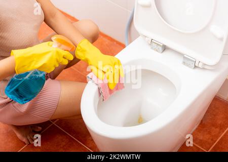 Hand einer asiatischen Frau, die den Toilettensitz mit Flüssigspray und einem rosa Tuch abwischte, um die Toilette im Haus zu reinigen Stockfoto