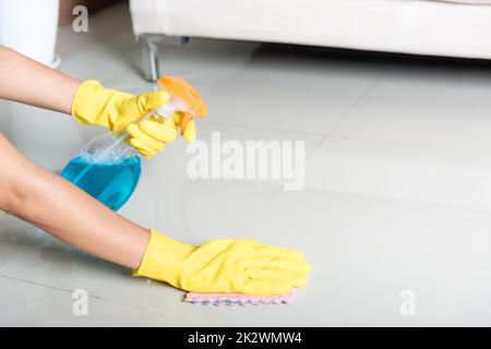 Eine Asiatin trägt einen gelben Gummi-glover mit Lappen und Reinigungsspray zu Hause Stockfoto