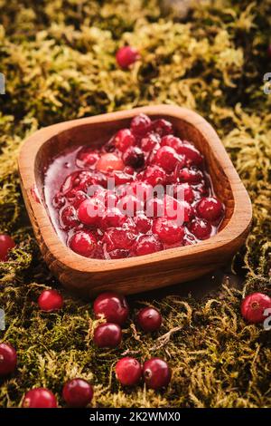 Preiselbeermarmelade in einer Holzschüssel auf einem Hintergrund aus Waldmoos. Stockfoto