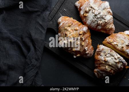 Gebackene Croissants auf einem Holzbrett und gestreut mit Puderzucker, schwarzer Tisch Stockfoto