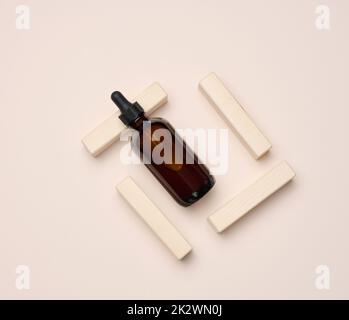 Braune Glasflasche mit Pipette auf beigem Hintergrund. Behälter für Kosmetika Stockfoto