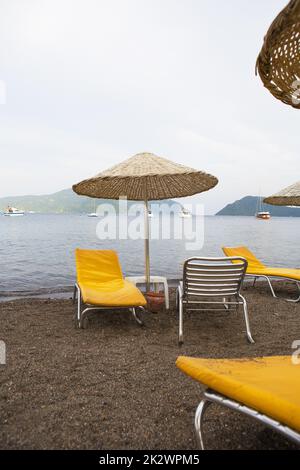 Wunderschöne gelbe Liegestühle und Sonnenschirme aus Stroh am Strand von Marmaris Stockfoto