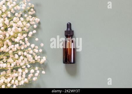 Blumen und Kosmetikflasche. Eine Glasflasche mit aromatischem Öl oder Serum mit Blumen in der Nähe. Natürliches organisches Spa-Kosmetikkonzept. Stockfoto