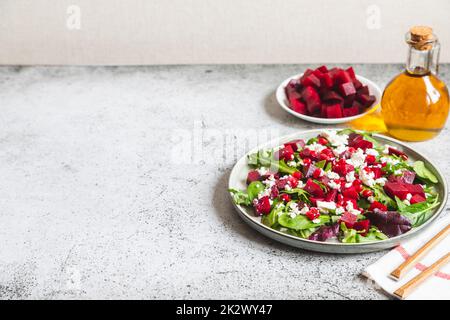 Rucola, Rüben- und Käsesalat mit Granatapfel und Dressing auf Teller auf grauem Stein Küchentisch Hintergrund, Platz für Text, Draufsicht Stockfoto