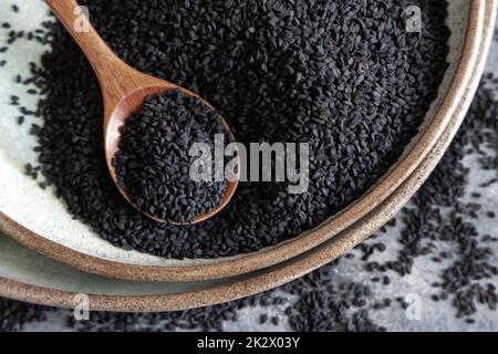 Teller mit indischem Gewürz Schwarzer Kreuzkümmel (Nigella sativa oder Kalonji), Nahaufnahme mit einem Holzlöffel Stockfoto