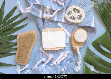 Handgemachte Seife auf blauem Badetuch in der Nähe von tropischen Blättern, Blick von oben, Modell Stockfoto