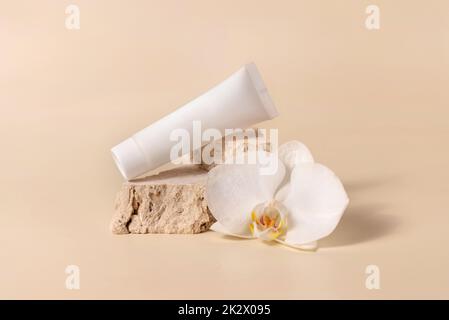 Weiße cremefarbene Röhre in der Nähe der weißen Orchideenblume auf hellgelb, Mockup. Hautpflegeprodukt Stockfoto