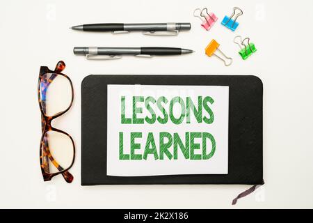 Text mit den gelernten Lektionen zur Inspiration. Geschäftskonzept fördern Sie den Austausch und die Nutzung von Kenntnissen aus Erfahrung Bürobedarf über Schreibtisch mit Tastatur, Gläsern und Kaffeetasse für die Arbeit Stockfoto