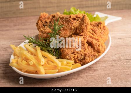Gebratenes Huhn und Kartoffelchip mit Rosmarinblatt, kalorienreiche Junk-Food auf weißem Teller serviert Stockfoto