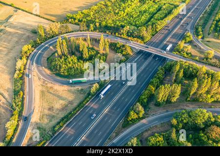 Autobahn aus der Vogelperspektive. Wenn die Sonne untergeht, erzeugen die Sonnenstrahlen wunderschöne lange Schatten auf dem Boden. Gelbe Bäume und umliegende Farmlan Stockfoto