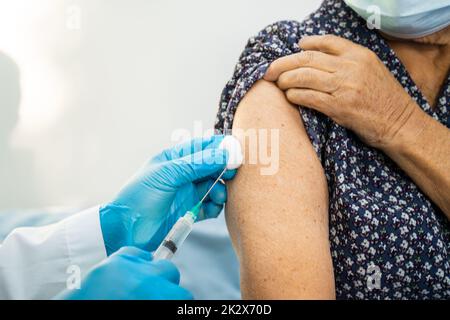 Ältere asiatische ältere Frau, die Gesichtsmaske trägt, erhält von einem Arzt eine Covid-19- oder Coronavirus-Impfung. Stockfoto