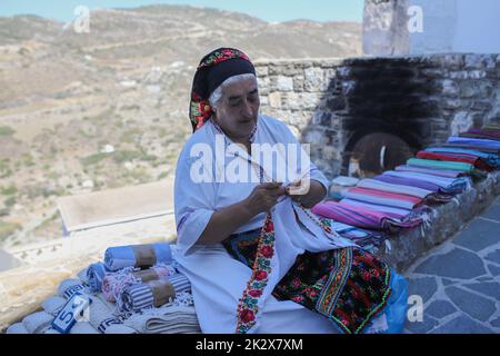 Frau Rigopoula außerhalb ihres Ladens mit lokalen handgewebten Textilien, traditionellen Schals und traditionellen Mini-Kostümen für Puppen, Olympos Dorf, Karpathos Insel. Karpathos ist die zweitgrößte Insel des griechischen dodekanischen Inselkomplexes in der südöstlichen Ägäis. Die Insel Karpathos hat immer noch ihre traditionelle Lebensweise, wie das Dorf Olympos, wo die Einheimischen noch immer die traditionellen Kostüme tragen. Stockfoto