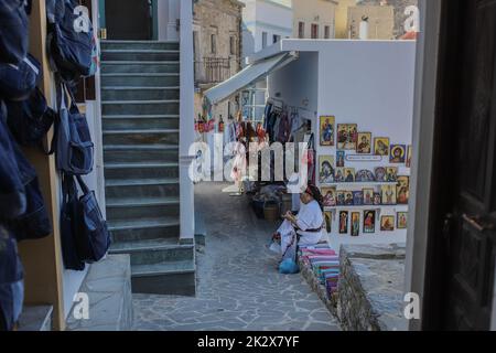 Frau Rigopoula außerhalb ihres Ladens mit lokalen handgewebten Textilien, traditionellen Schals und traditionellen Mini-Kostümen für Puppen, Olympos Dorf, Karpathos Insel. Karpathos ist die zweitgrößte Insel des griechischen dodekanischen Inselkomplexes in der südöstlichen Ägäis. Die Insel Karpathos hat immer noch ihre traditionelle Lebensweise, wie das Dorf Olympos, wo die Einheimischen noch immer die traditionellen Kostüme tragen. Stockfoto