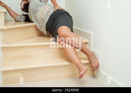 Asiatische Dame Frau Verletzungen durch Herunterfallen auf rutschigen Oberflächen Treppen zu Hause. Stockfoto