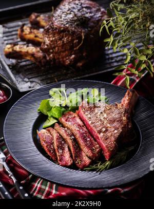 Steak auf den Knochen. Rib-Eye. Tomahawk Steak auf dem schwarzen Teller mit Rosmarin. Rösten - Selten. Entrecote Stockfoto