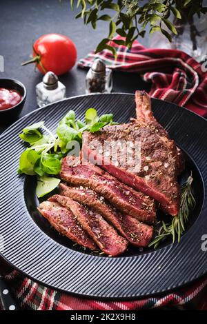 Steak auf den Knochen. Rib-Eye. Tomahawk Steak auf dem schwarzen Teller mit Rosmarin. Rösten - Selten. Entrecote Stockfoto