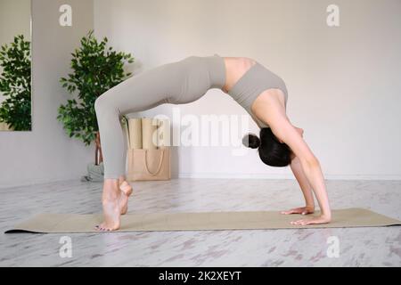 Eine junge schöne Frau praktiziert Yoga im Studio, steht in einer Bogenpose. Stockfoto