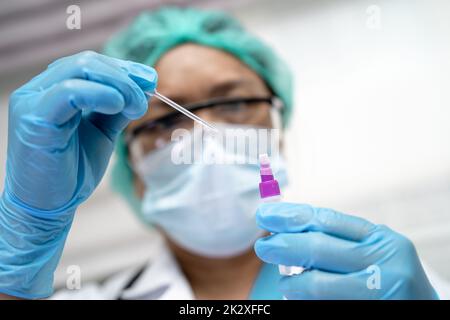 Asiatischer Arzt im PSA-Anzug mit Speichelantigen-Testkit zur Kontrolle des Covid19-Coronavirus im Krankenhaus. Stockfoto