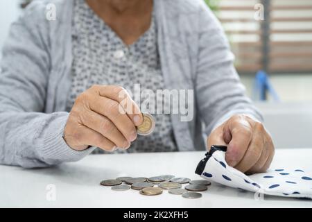 Asiatische ältere oder ältere alte Dame, die das Münzgeld in der Tasche hält. Armut, Sparproblem im Ruhestand. Stockfoto