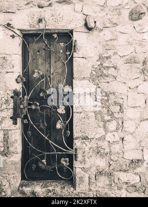 Alte Holztür eines Steinhauses mit einem dekorierten Metalltor Stockfoto