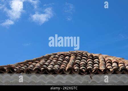 Alte traditionelle Fliesen, die das Dach eines Hauses mit einer weißen Fassade bedecken. Strahlend blauer Himmel mit hellweißen Wolken. Lanzarote, Kanarische Inseln, Spanien. Stockfoto