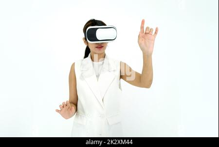 Asiatische Frau in weißem Kleid mit Virtual-Reality-Brille, spielen ein interaktives Spiel. Konzept Der Zukunftstechnologie. Stockfoto