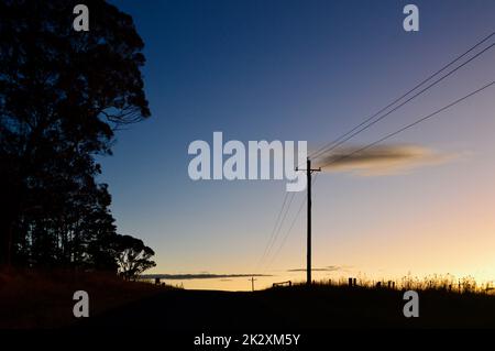 Strommasten an einer Landstraße bei Sonnenuntergang Stockfoto