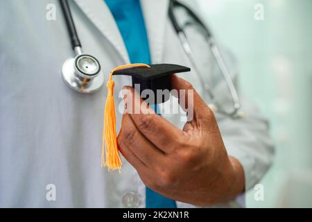 Asiatische Frau Arzt hält Abschlusshut im Krankenhaus, Medizinische Ausbildung Konzept. Stockfoto