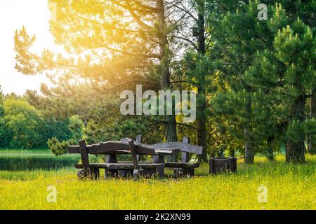 Rustikaler Holztisch und Bänke am Ufer eines ruhigen Flusses oder Sees Stockfoto