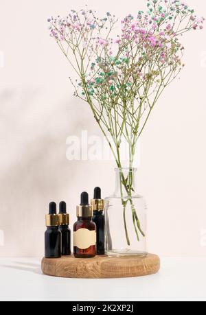 Glasbraune Flasche mit Pipette auf einem Holzpodium und einem Blumenzweig. Stockfoto