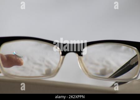 Blaue Kontaktlinse durch die schwarze Brille zeigt verschiedene Brillen, um durch Optometrie Weitsicht und Kurzsichtigkeit zu korrigieren, oder Augenarzt gegen Myopie mit Augenkorrektur für perfektes Sehen Stockfoto