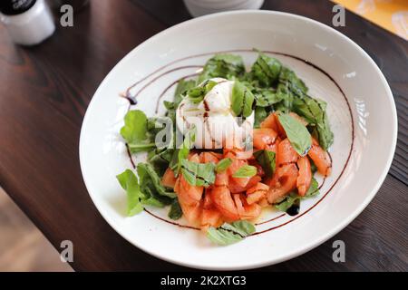 Caprese Salat auf einem runden weißen Teller. Auf einem modernen Holztisch. Selektiver Fokus. Stockfoto