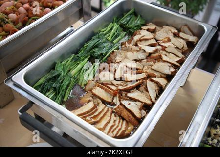 Schweinebraten mit Gemüse, Speisen in Buffetform. Der Behälter besteht aus einem rechteckigen Edelstahl-Tablett. Selektiver Fokus. Stockfoto