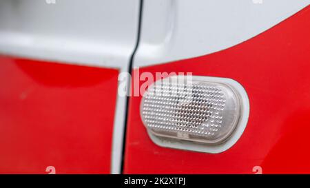 Kfz-Glühlampe. Blinker an der Seite des Fahrzeugs. Ein weißer Blinker an einem roten Kreuz, der sich auf der rechten Seite der Kotflügeloberfläche befindet. Stockfoto