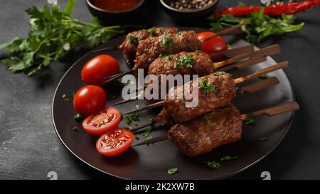 Shish Kebab ist eine beliebte Mahlzeit aus Spieß- und gegrillten Fleischwürfeln. Gerösteter Rinderkebab auf einem Holzspieß mit Gewürzen, Kräutern und Tomaten Stockfoto