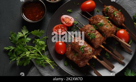 Shish Kebab ist eine beliebte Mahlzeit aus Spieß- und gegrillten Fleischwürfeln. Gerösteter Rinderkebab auf einem Holzspieß mit Gewürzen, Kräutern und Tomaten Stockfoto