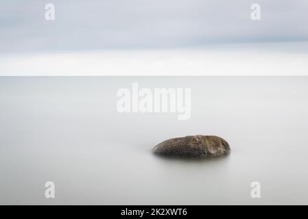 Das Meer wäscht die großen Steine gegen den rosa Sonnenuntergang. Die verwendete Technik - Langzeitbelichtung. Stockfoto